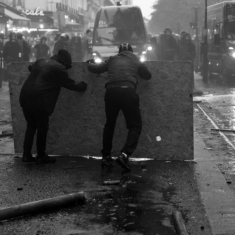 Paris, octobre 2026 : des manifestants se mettant à l'abri  font face à des gendarmes.