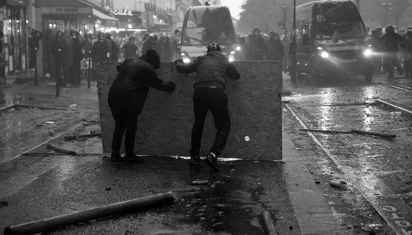 Paris, octobre 2026 : des manifestants se mettant à l'abri  font face à des gendarmes.