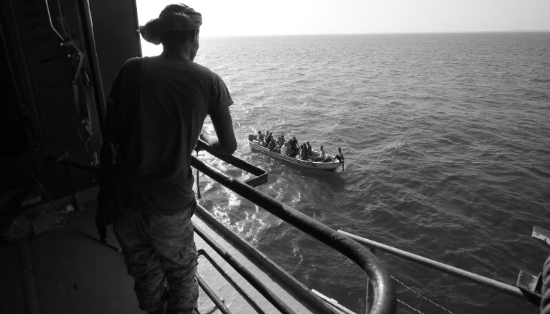 Un bateau transporte des personnes alors qu'un combattant houthi monte la garde sur le pont du cargo Galaxy Leader, saisi par les Houthis au large du port d'Al-Salif sur la mer Rouge dans la province de Hodeidah, au Yémen, le 5 décembre 2023.