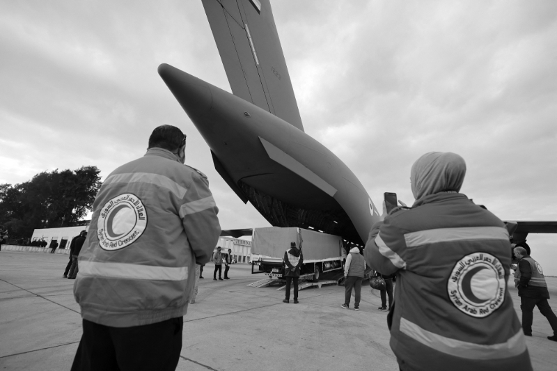 Des employés du Croissant rouge syrien observent un avion militaire transportant du matériel et des secouristes des Emirats arabes unis qui arrive à l'aéroport international de Damas, le 9 février 2023, après le séisme meurtrier qui a frappé la Syrie et la Turquie.